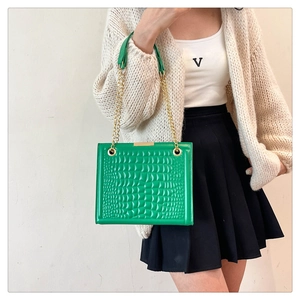 Detailed view of a green crocodile embossed tote bag with gold chain strap on a model