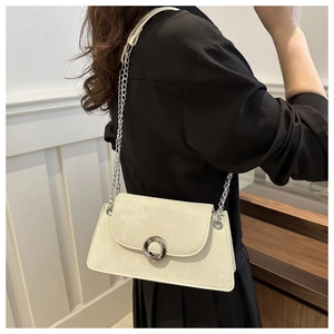 Détail d'un sac bandoulière crème avec chaîne argentée porté sur une tenue noire