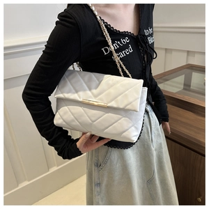 Detail of white quilted crossbody bag with golden metal lock and chain strap on model