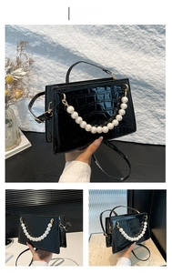 Detail of black faux crocodile leather handbag with elegant pearl handle and gold hardware