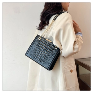 Detailed shot of black crocodile embossed shoulder bag with gold chain strap worn by a model