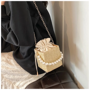 Detail of woven straw bucket bag featuring a large pearl handle and golden chain strap