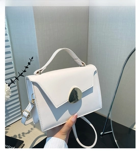Detail of white square bag with golden shield buckle and smooth leather texture