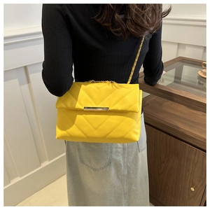 Detail of yellow quilted chain bag with V-shaped stitching and gold metallic hardware