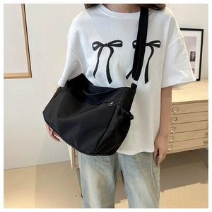 Close-up of minimalist black nylon crossbody bag with drawstring side detail and wide strap