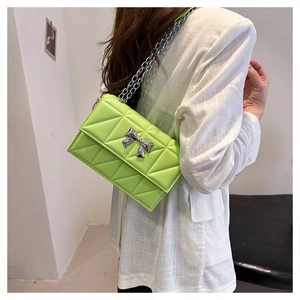Gros plan d'un sac matelassé vert citron avec nœud argenté sur blazer en lin