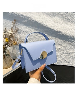 Detail of light blue crossbody bag featuring a golden pebble buckle and envelope flap design
