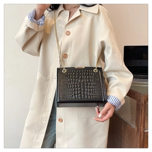 Chic black crocodile pattern tote bag with gold chain strap worn with a beige trench coat
