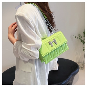 Sac matelassé vert fluo avec nœud argenté porté par un mannequin sur une chemise blanche