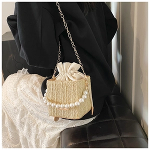 Detail of woven straw bucket bag with large pearl handle and golden chain shoulder strap