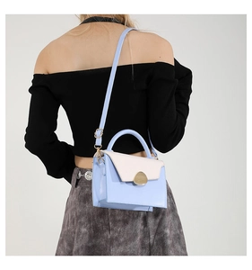 Detail view of light blue and white color-block handbag worn by model for size scale