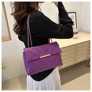 Close-up of a purple quilted chain bag worn by a model in a minimalist indoor setting