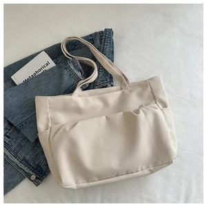 Détail du fourre-tout en toile beige avec poche avant sur fond en tissu texturé