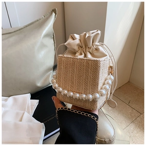 Detail view of woven straw bucket bag with large pearl handle and leather drawstring