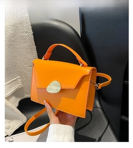 Detail of orange patent leather crossbody bag with distinctive metallic buckle and top handle