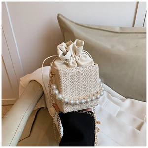 Detail of woven mini bucket bag with oversized pearl handle and golden chain strap