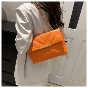 Detail of orange quilted crossbody bag featuring V-shaped stitching and gold chain strap