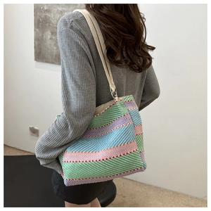 Detail of multi-color woven tote bag with white faux leather straps and silver rings
