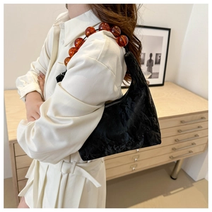 Detail of black pleated shoulder bag with amber beaded chain on a minimalist background