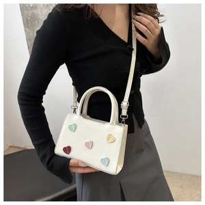 Detail of mini crossbody bag showing colorful heart patches and embossed fashion logo