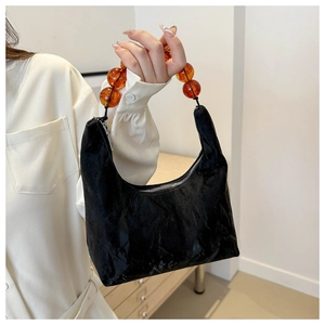 Detail of a black velvet handbag with amber-colored bead handle and metal zipper closure