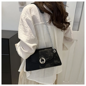 Détail du sac noir bi-matière avec boucle argentée et bandoulière chaîne sur modèle