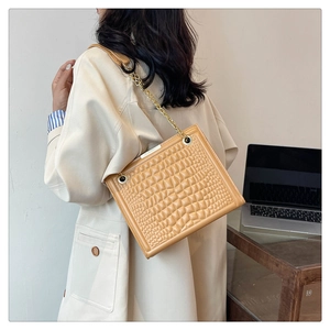 Detail of tan crocodile embossed texture on a crossbody bag with a gold chain strap