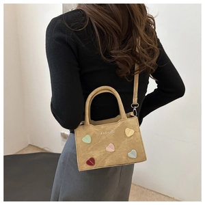 Detailed view of a brown suede bucket bag with colorful heart patches and fashion text