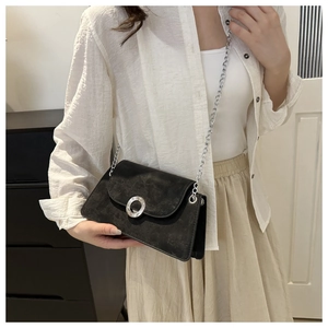 Détail d'un sac bandoulière en daim noir avec boucle métallique argentée et bandoulière chaîne