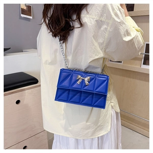Sac bandoulière bleu matelassé avec nœud argenté et chaîne porté par un mannequin