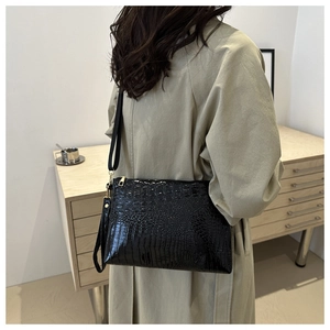 Detail of a large black crocodile pattern shoulder bag on a model in a minimal room