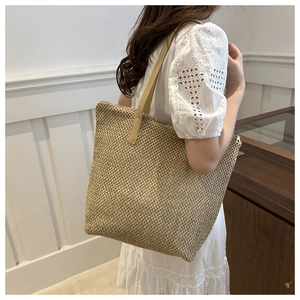 Dettaglio della borsa tote in paglia intrecciata con spalline in pelle marrone su abito