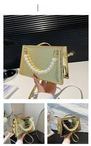 Detail view of gold crocodile embossed square bag with dual pearl handle and metallic finish