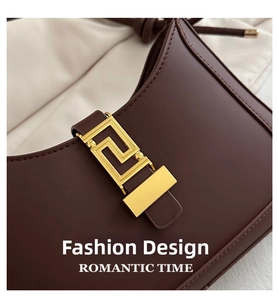 Detail of a dark brown leather crescent bag with a gold geometric meander metal buckle