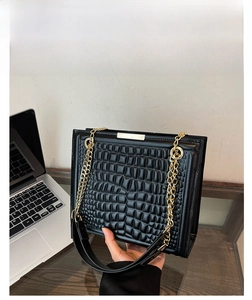 Close-up of black crocodile pattern leather tote bag with gold chain and metal clasp