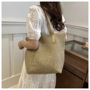 Dettaglio della borsa tote in paglia intrecciata a mano con tracolla su abito bianco