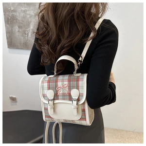 Detail of red and green plaid backpack featuring pink bow embroidery and leather straps