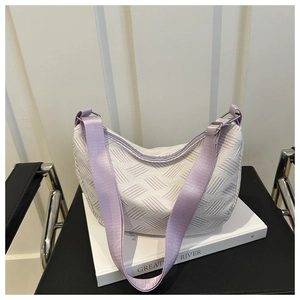 Detail of white textured hobo bag with purple nylon strap and metal buckle on books