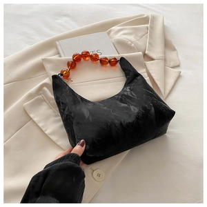 Detail of black crescent hobo bag featuring amber resin bead handle on beige blazer