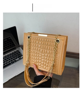 Detail of khaki crocodile pattern leather bag with gold chain and laptop as background