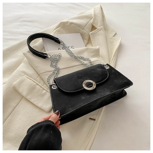 Détail d'un sac bandoulière noir avec boucle anneau argenté et chaîne sur blazer beige