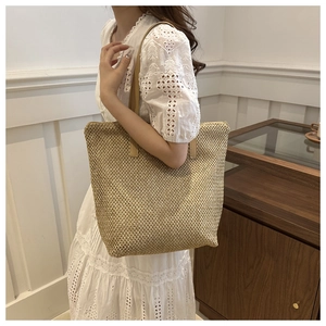 Dettaglio della borsa tote in paglia intrecciata con tracolla in pelle su abito bianco