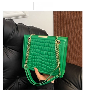 Detail of green faux leather tote bag with crocodile pattern and gold chain strap
