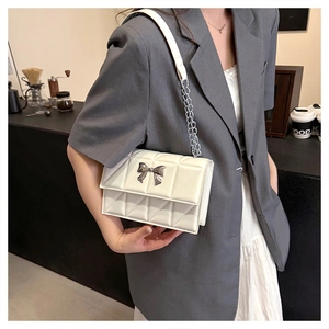 Gros plan d'un sac bandoulière blanc matelassé avec boucle nœud argenté en café