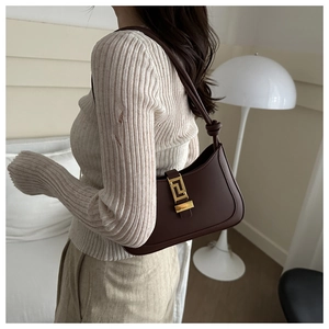 Detail of a dark brown half-moon underarm bag with a golden geometric metal buckle