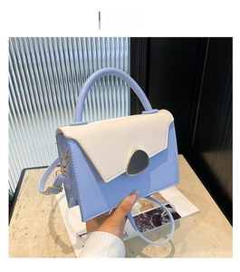 Close-up of a blue and cream leather handbag featuring a grey pebble-shaped gold buckle
