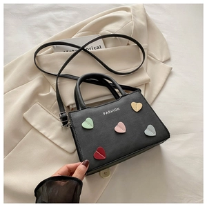 Detail of black handbag with colorful heart patches and white Fashion text on blazer
