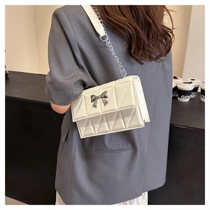 Détail du sac bandoulière matelassé blanc avec nœud argenté et bandoulière chaîne