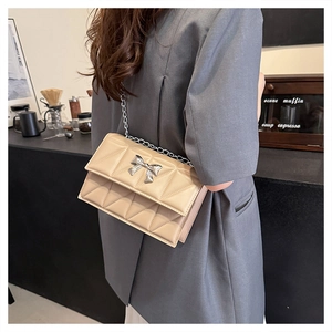 Détail d'un sac bandoulière beige matelassé avec boucle nœud argentée et chaîne élégante