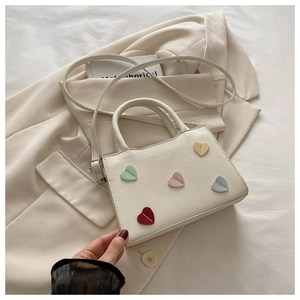 Detail of cream bucket bag with colorful stitched hearts and fashion text on surface